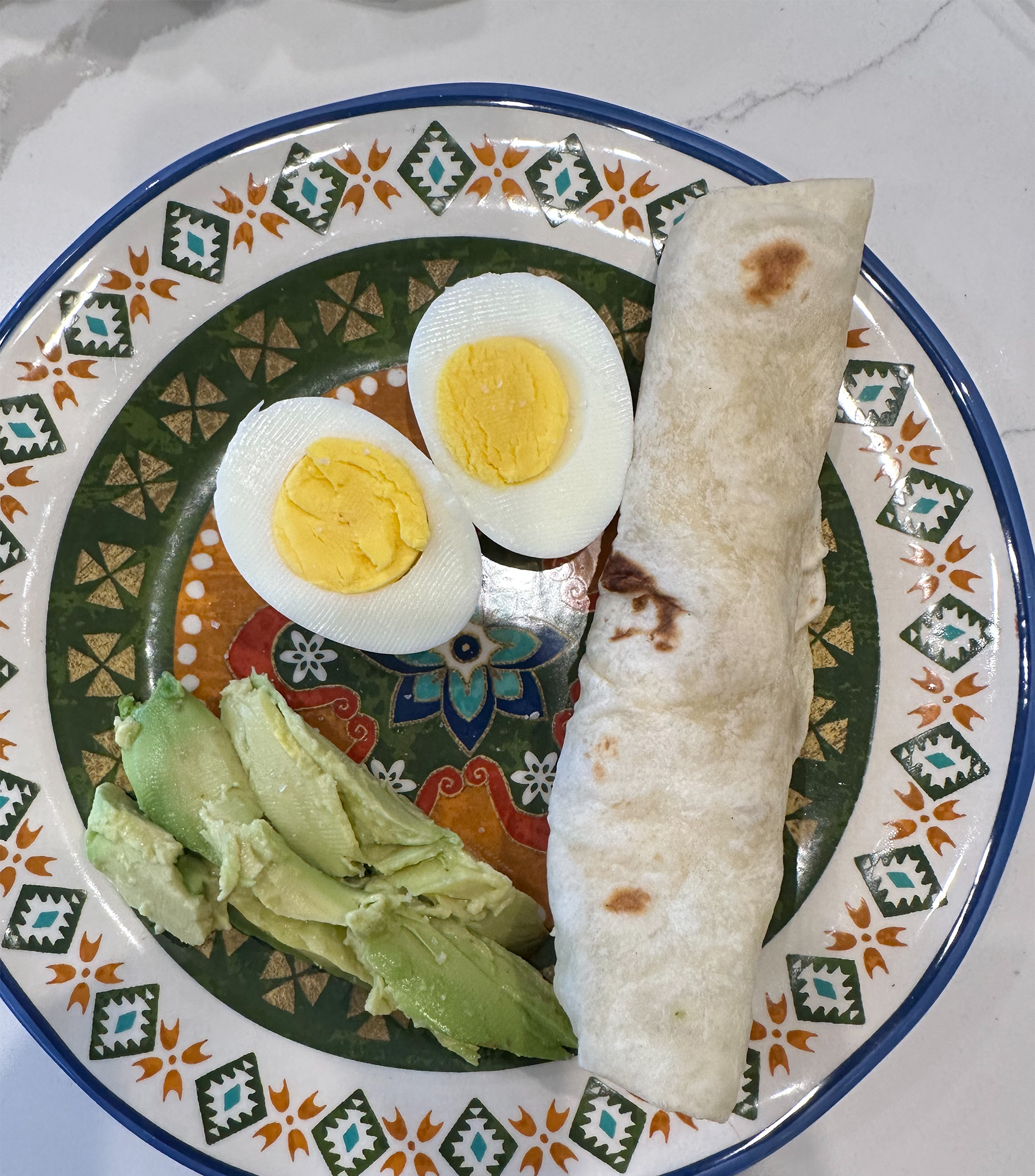 A plate with boiled egg, flour tortilla rolled up and avocado